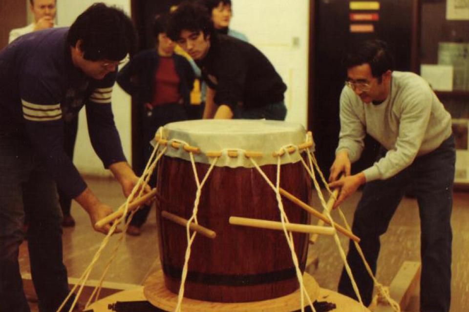 Three people tighten the tension on a drum head